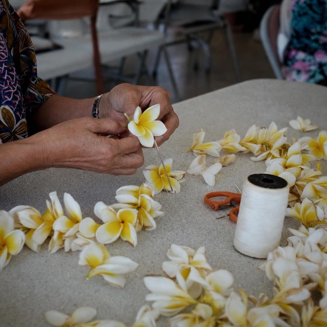 Hands arranging flowers at a guided lei-making table