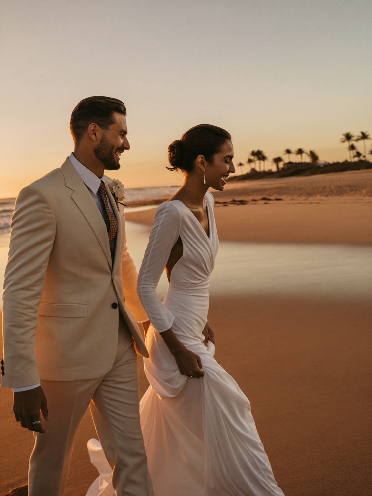 Bride and groom walking the shoreline at golden hour, seen in profile